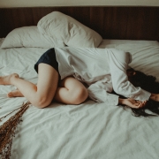 A woman experiencing constipation lying on a bed, covering her face